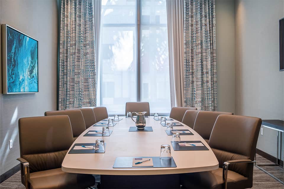 Conference room with long table, leather chairs, and large windows with blue artwork on wall