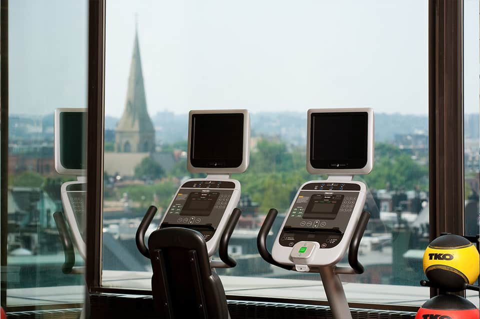 Exercise bikes at floor-to-ceiling windows overlooking a city with a church spire