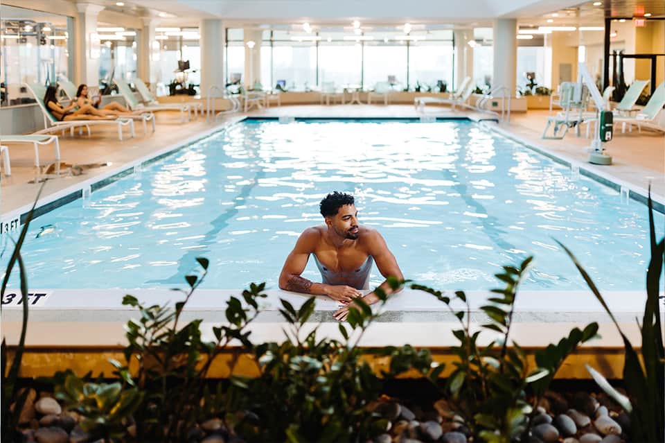 Indoor lap pool with bright skylights, man in water, lounge chairs, and large windows