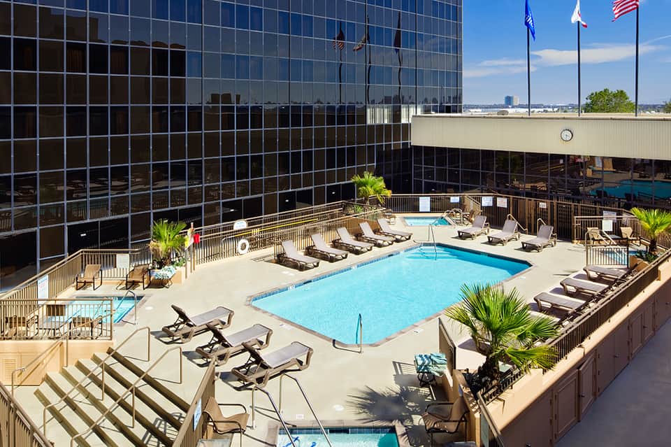 Resort pool deck with loungers, umbrellas, and high-rise building with city views