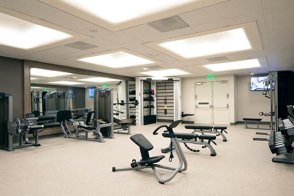 Bright fitness center with exercise equipment, weights, and TV screen