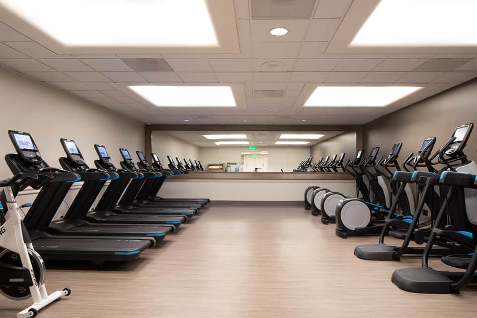 Spacious fitness facility with rows of treadmills on both sides, blue accents, and recumbent bikes