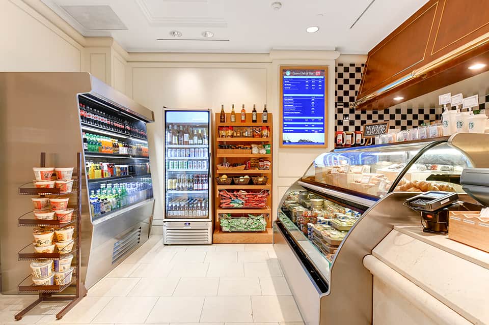 Modern hotel cafe interior with refrigerated display cases, beverage coolers, pastry shelves, and checkered tile backsplash