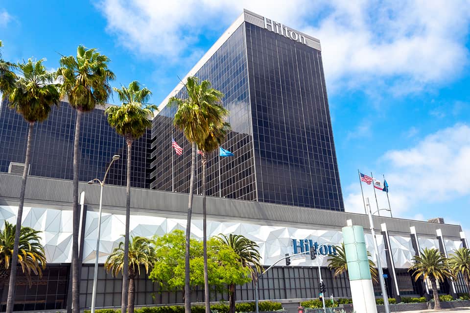 Hilton hotel exterior with dark facade, palm trees, and white entry canopy with flags