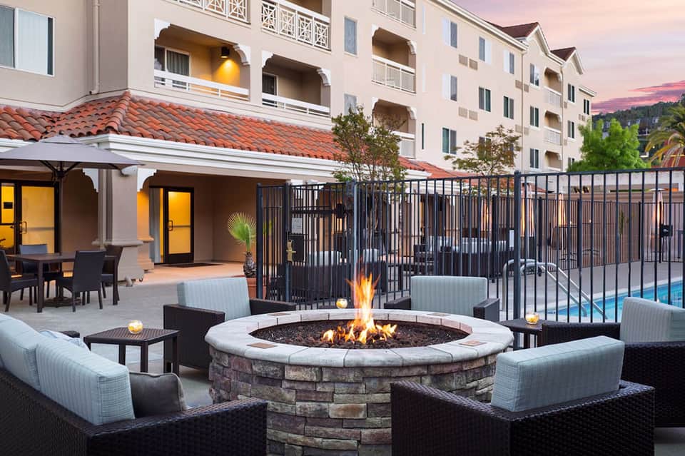 Outdoor fire pit seating area with fireplace, lounge chairs, and resort buildings at dusk