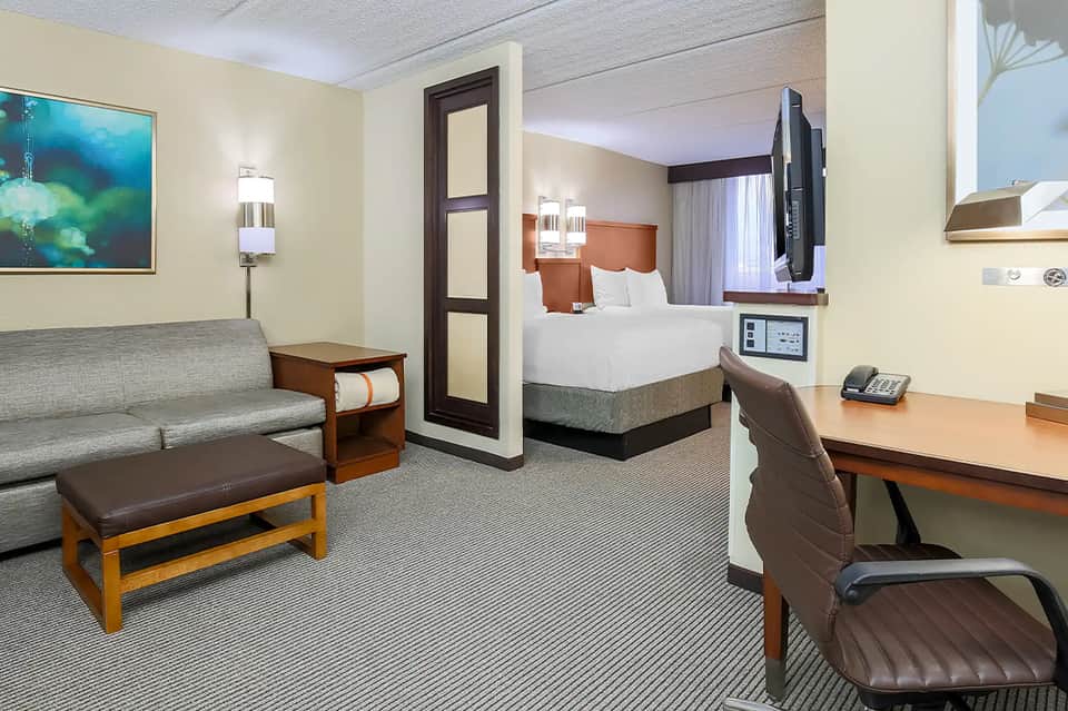 Modern hotel suite with queen bed, sofa, desk workspace, and contemporary furnishings
