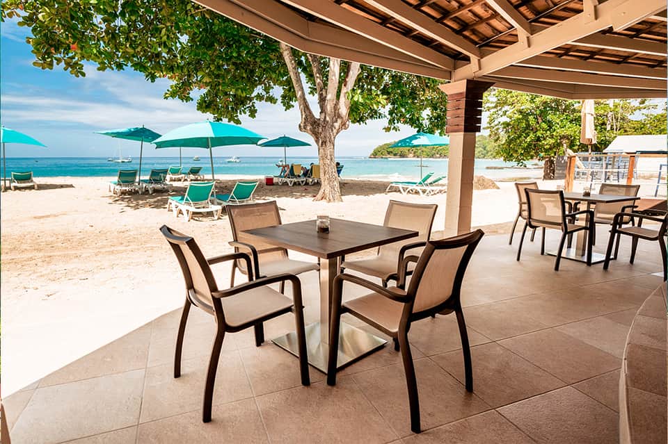 Beachfront dining patio with turquoise umbrellas, lounge chairs, and ocean views
