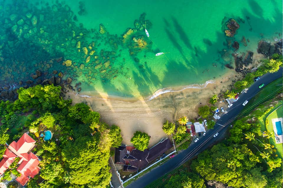 Aerial view of pristine beach cove surrounded by lush green forest with turquoise water