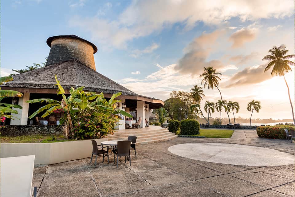 Tropical resort building with distinctive conical thatched roof surrounded by palm trees and waterfront
