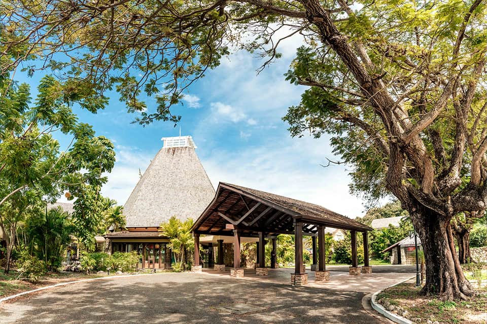 Tropical resort building with distinctive pyramid roof, wooden pergola entrance, and mature shade trees
