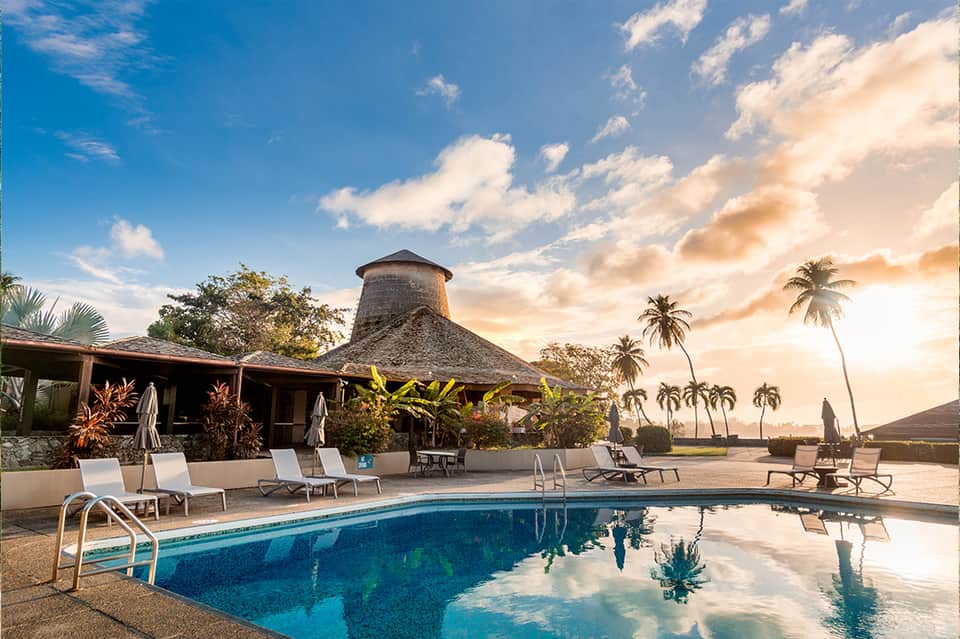 Resort pool with thatched-roof pavilion, palm trees, and tropical landscape at golden hour