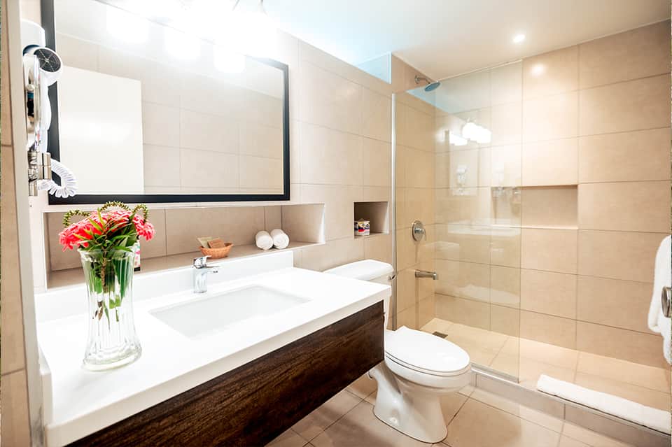 Modern bathroom with beige tile walls, floating vanity, large mirror, and glass-enclosed shower area
