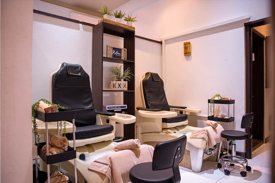 Spa pedicure station with black leather chairs, footbaths, and decorative plants in a pink and beige room