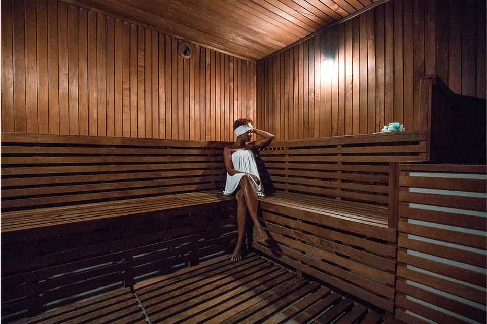 Person relaxing on wooden bench in a sauna with vertical wood paneling and horizontal slat seating
