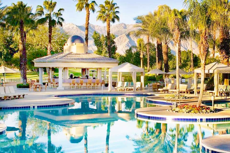 Resort pool with gazebo pavilion, palm trees, and mountain backdrop in desert landscape