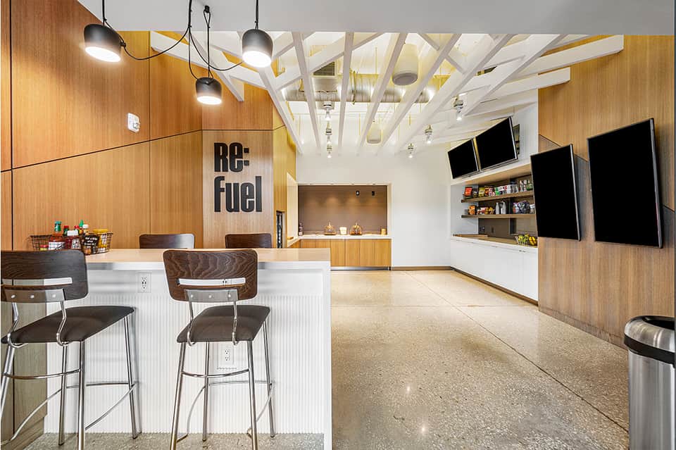 Modern hotel lobby with wood paneling, bar seating, and digital displays