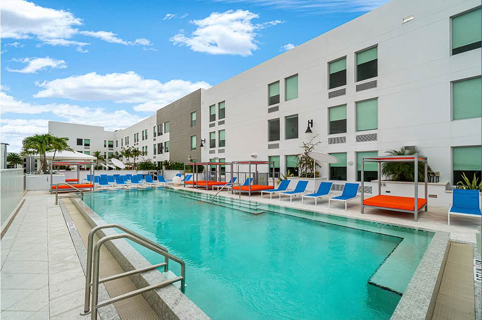 Contemporary pool deck with turquoise water, blue loungers, and white modern hotel building