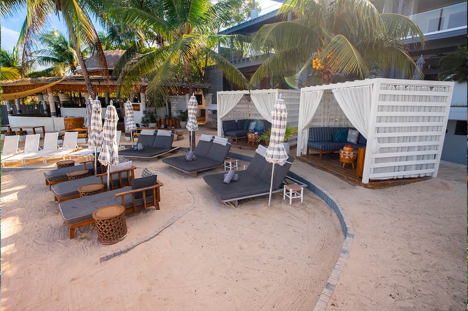 Beach club with white cabana tents, black lounge chairs, and palm trees