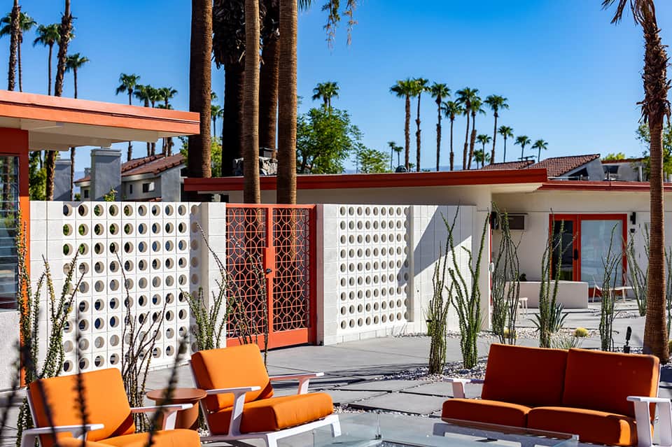 Mid-century modern courtyard with orange furniture, decorative white wall panels, and palm trees