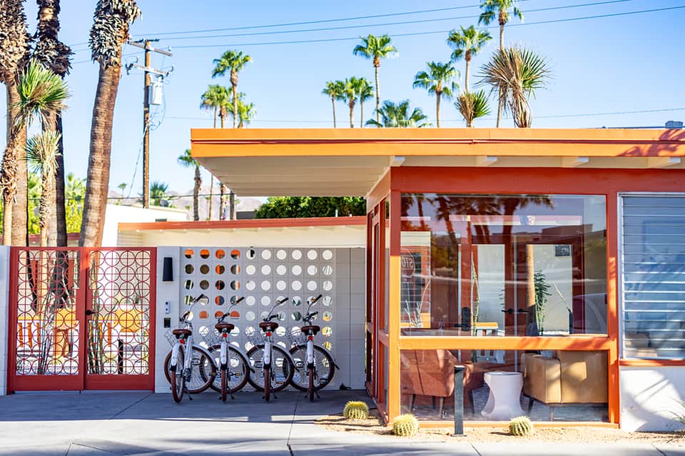 Mid-century modern building with orange and yellow exterior, palm trees, and bike rentals