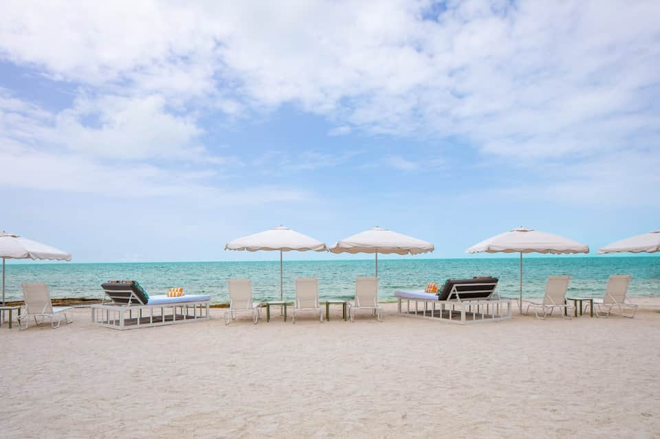 Beach lounge setup with white umbrellas, sun chairs, and turquoise ocean water