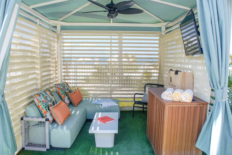 Covered outdoor lounge with light blue ceiling, striped privacy screens, seating area, cushions, and ceiling fan