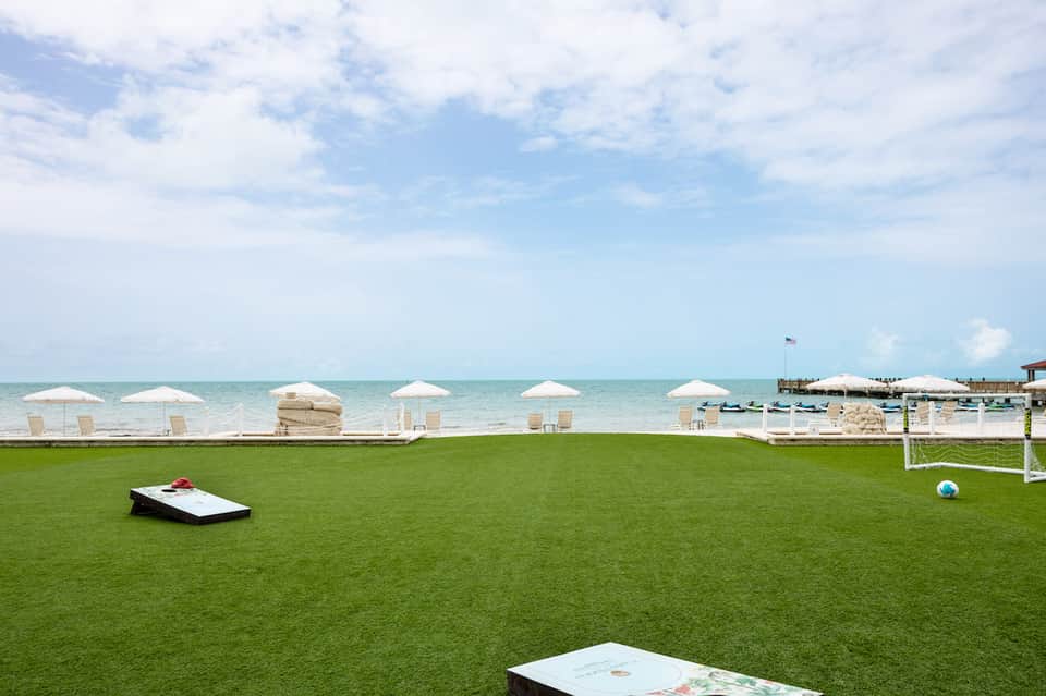 Manicured lawn with white umbrellas, lounge chairs, and cornhole games overlooking the ocean