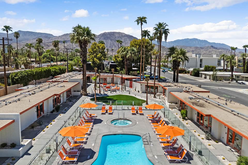 Resort pool deck with blue swimming pool, orange lounge chairs, umbrellas, and desert mountain views