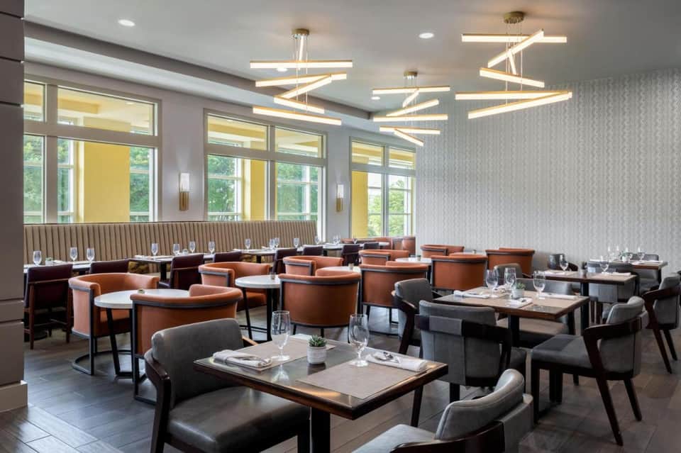 Modern restaurant dining room with orange chairs, geometric light fixtures, and large windows