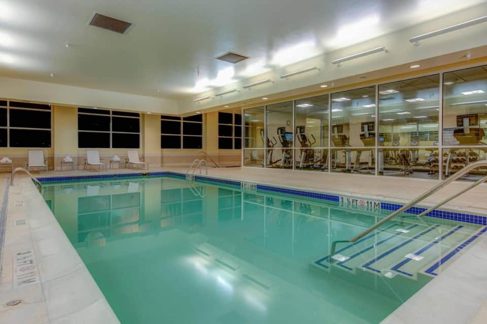Indoor swimming pool with chlorine-treated water and fitness facility visible through glass