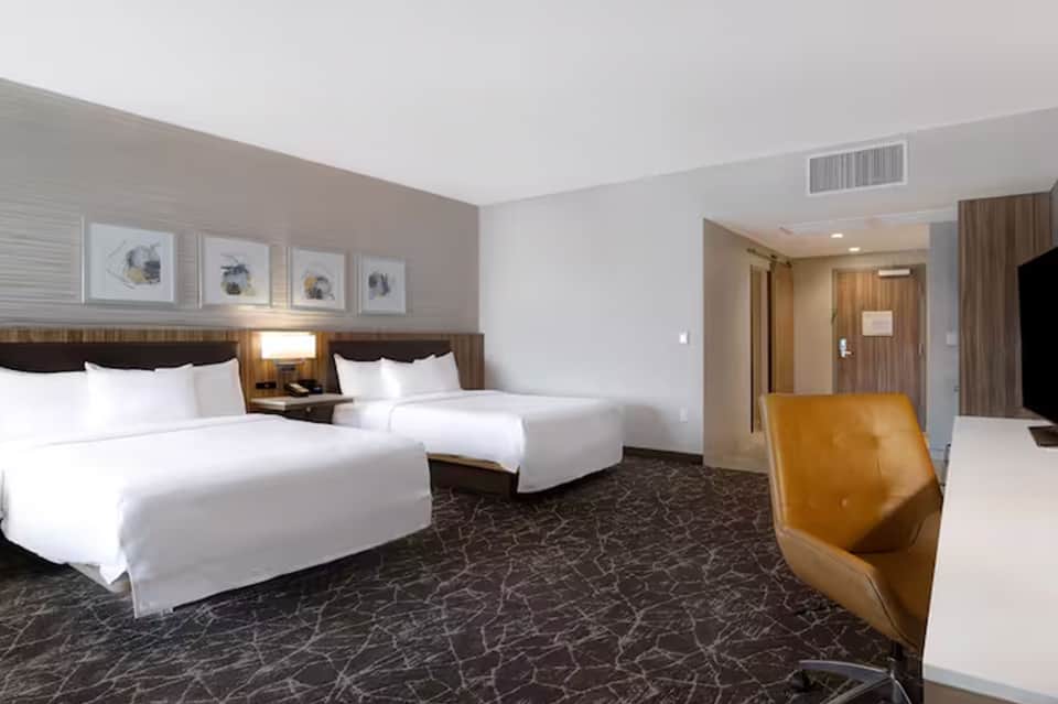 Modern hotel room with two queen beds, neutral décor, and contemporary furnishings