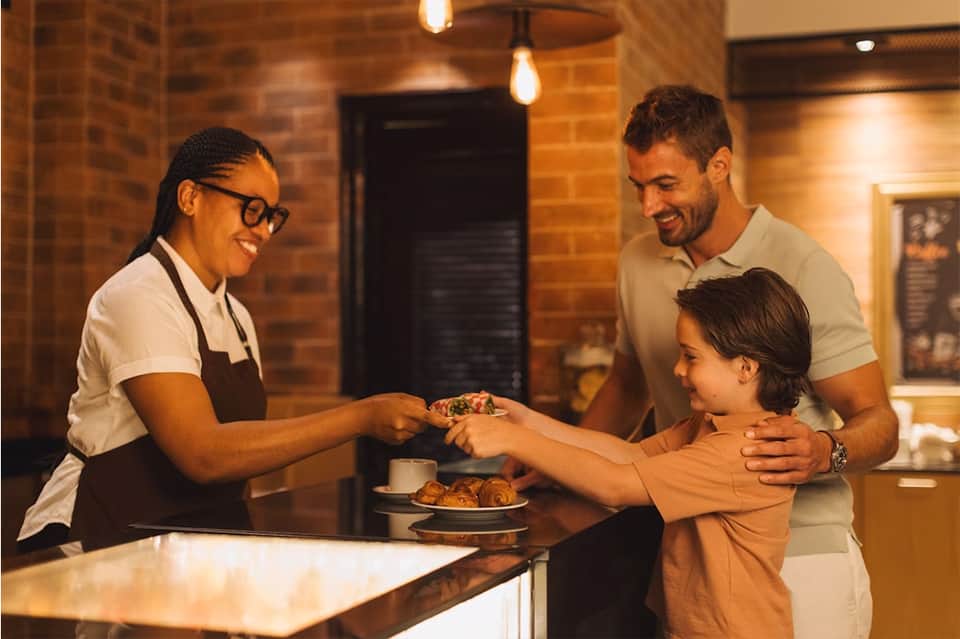 Restaurant server handing pastry to young child while parent watches in warm brick interior
