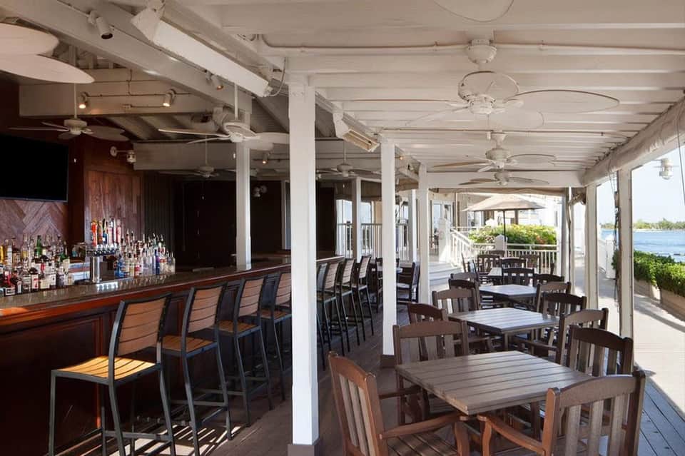Waterfront restaurant with bar, wooden tables, white columns, and covered patio overlooking water and boats