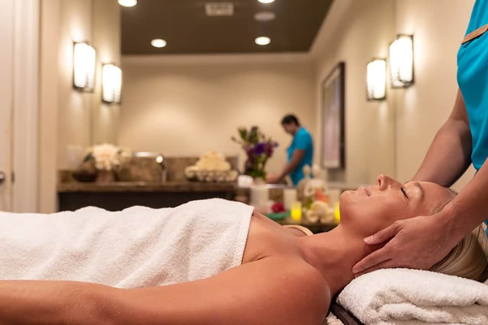 Spa therapist giving neck massage to client in luxury spa room with ambient lighting