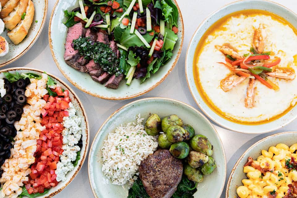 Overhead view of colorful plated dishes including steak salad, seafood, pasta, and various appetizers