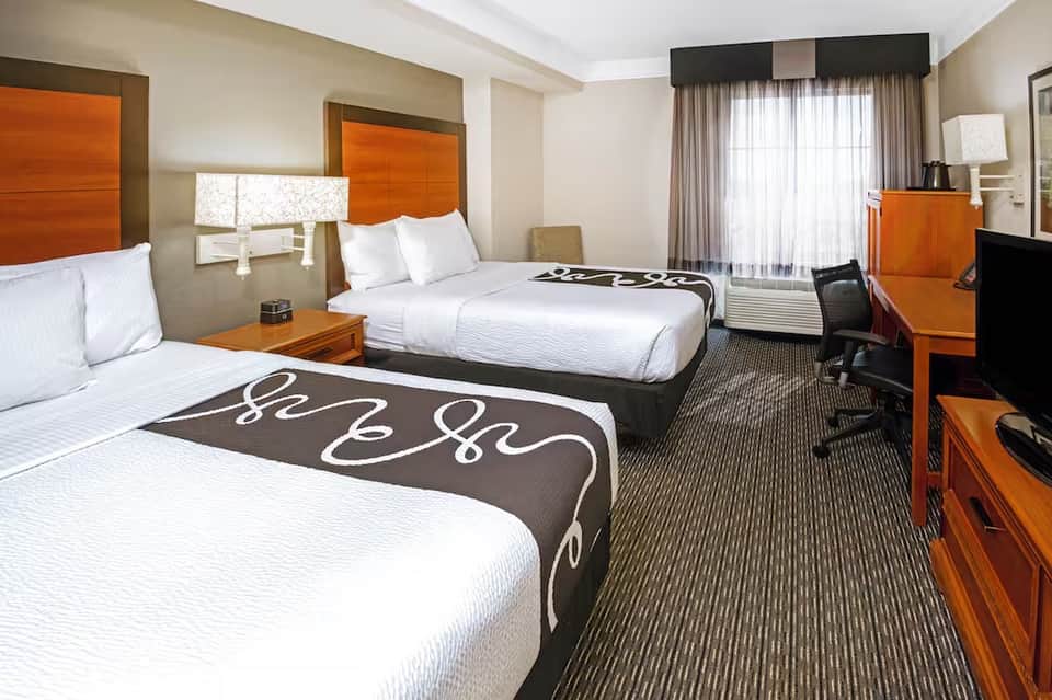 Modern hotel room with two queen beds, orange headboards, desk area, and contemporary furnishings