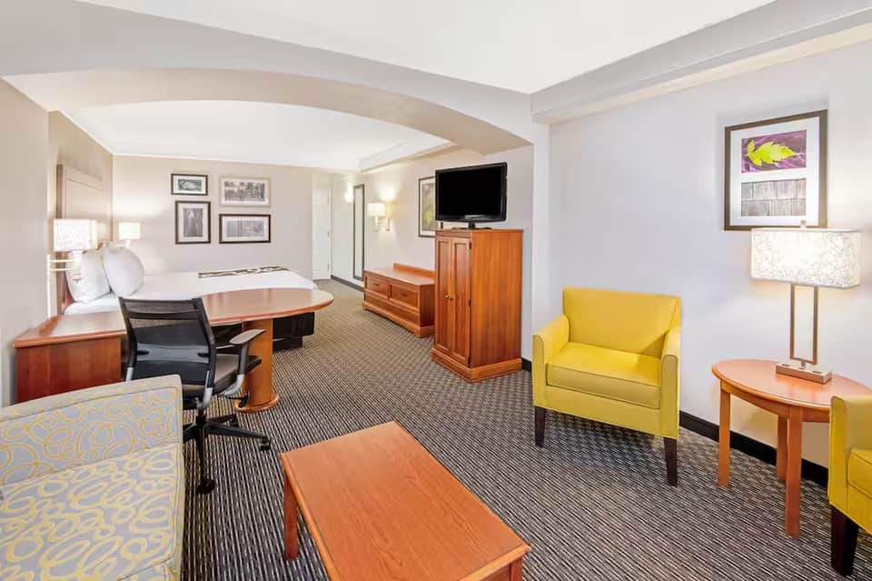 Spacious hotel suite with king bed, yellow accent chair, wood furniture, and curved ceiling details