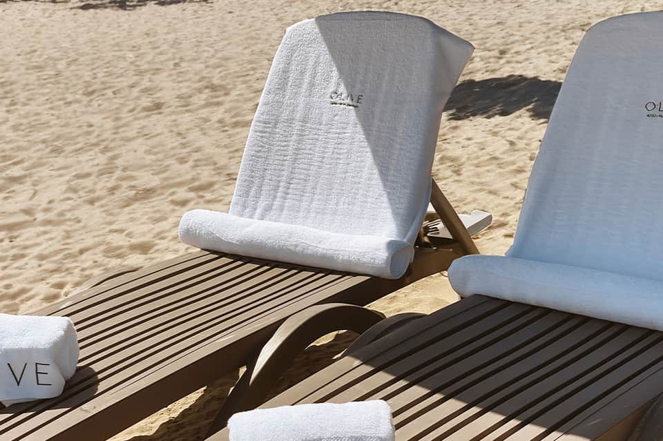 Beach lounge chairs with white towel covers lined up on sandy beach