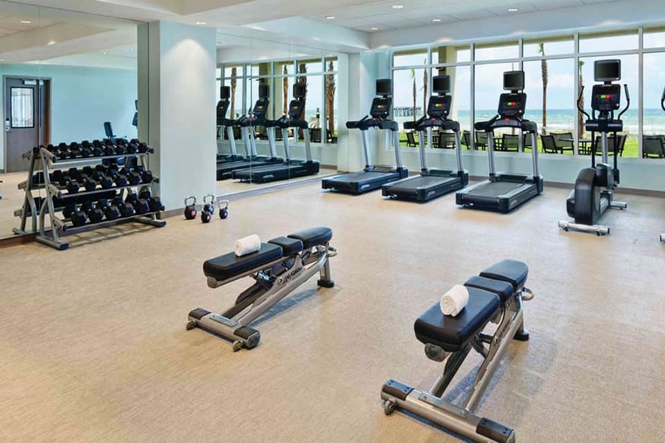 Modern fitness center with treadmills, exercise bikes, dumbbells, and ocean views through large windows