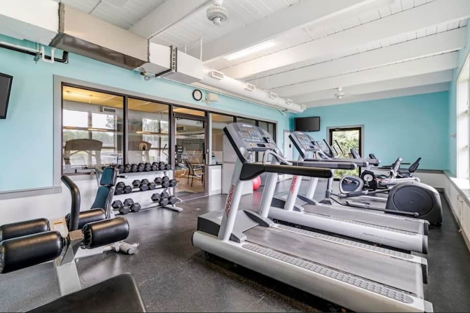 Modern gym with treadmills, exercise bikes, dumbbells, and turquoise accent walls