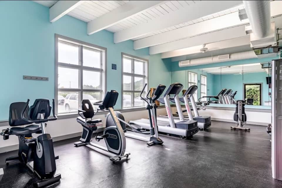 Bright turquoise fitness center with exercise bikes, treadmills, large windows, and mirrored walls