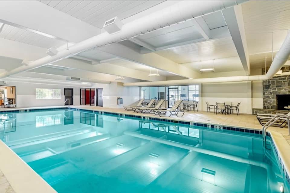 Indoor swimming pool with high ceilings, lounge chairs, and stone fireplace