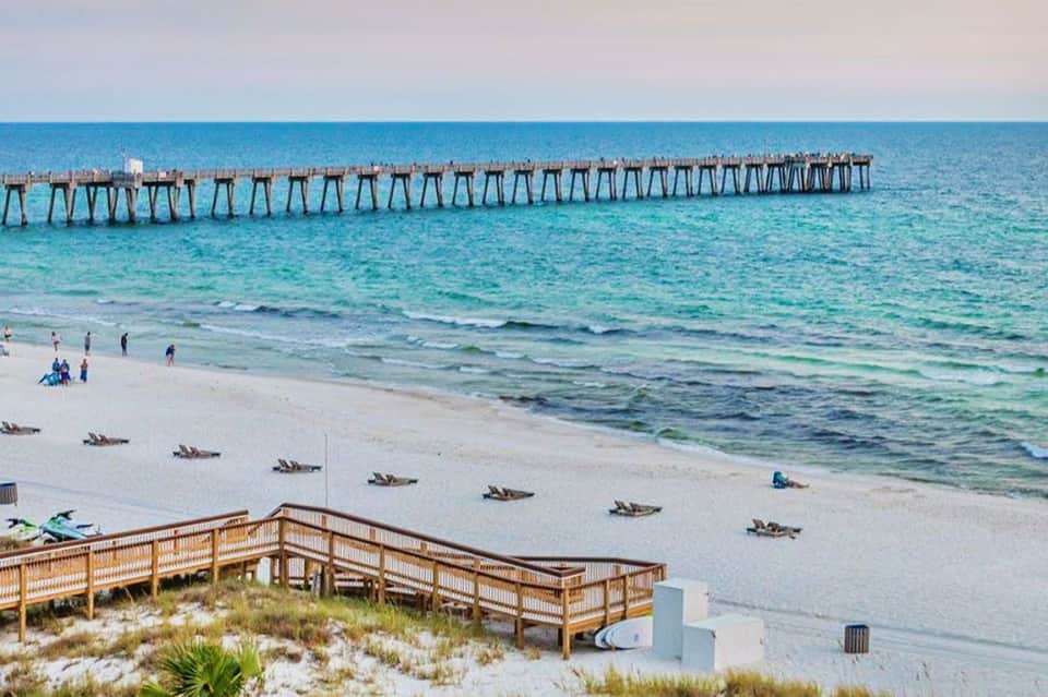 Wooden pier extending into turquoise ocean water with sandy beach and dunes in foreground