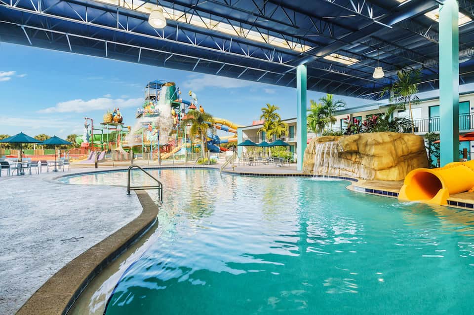 Indoor water park with slides, splash pad, and lazy river under metal roof structure