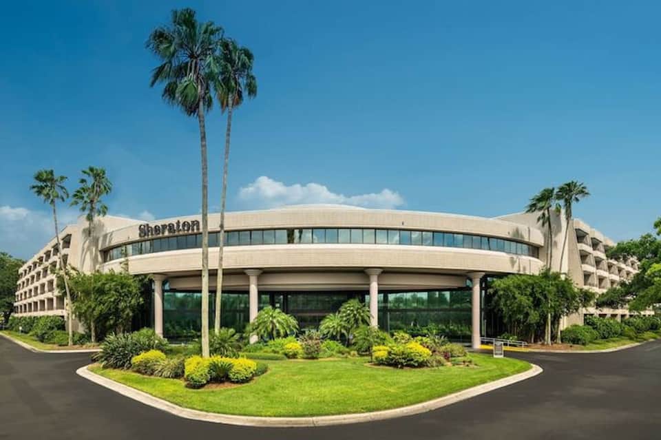 Sheraton hotel exterior with curved facade, palm trees, and manicured landscaping