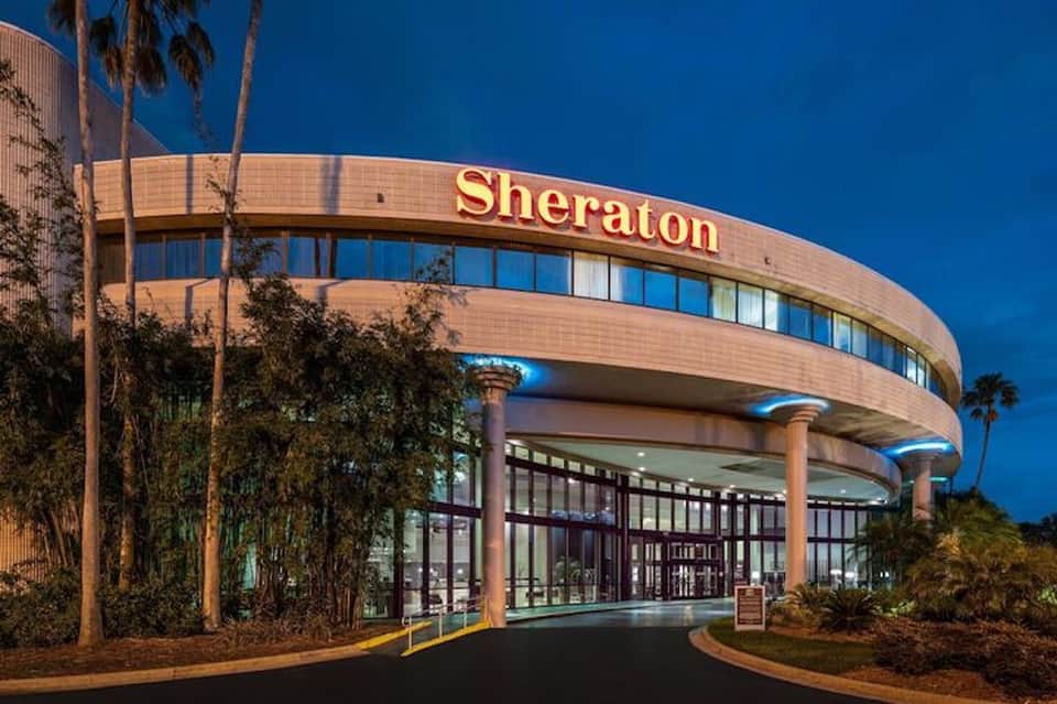 Curved Sheraton hotel entrance with terracotta brick facade, glass doors, and palm trees at dusk