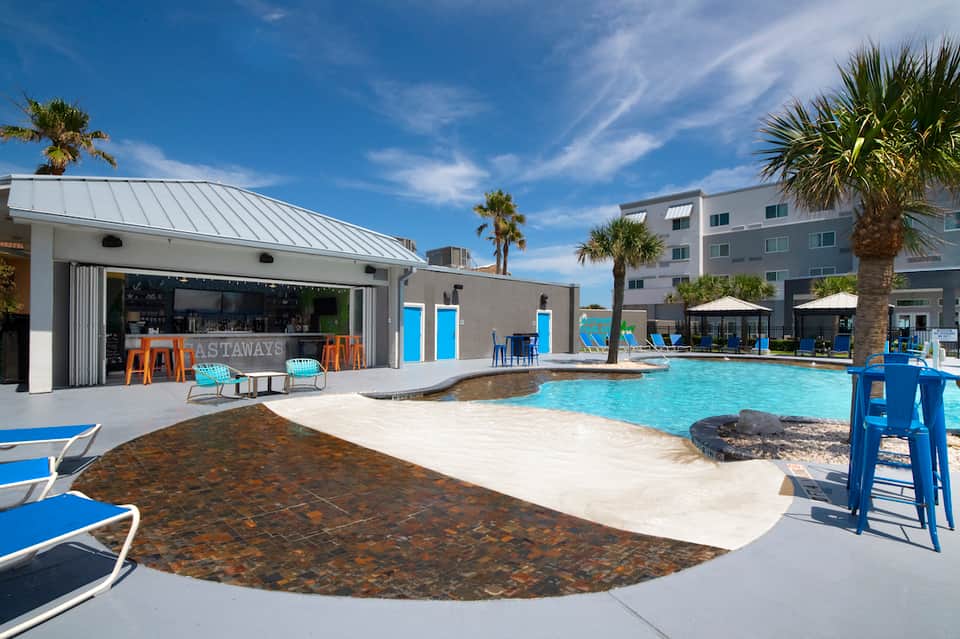 Contemporary resort pool with blue loungers, modern cabana, and palm trees during daytime