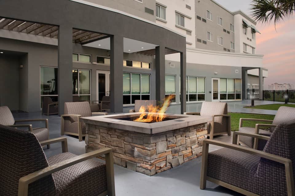 Outdoor fire pit seating area with gray woven chairs and modern building facade at dusk