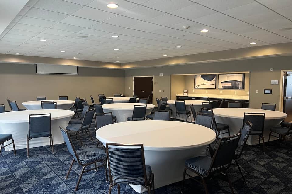 Modern conference room with round white tables, black chairs, recessed lighting, and kitchenette