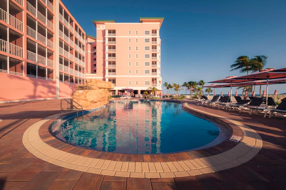 Beachfront resort with curved swimming pool, multi-story accommodation buildings, and ocean view deck